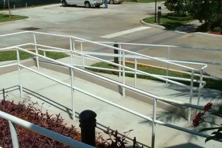Accessible ramp leading to business entrance with compliant handrails and sidewalk crossing visible in background