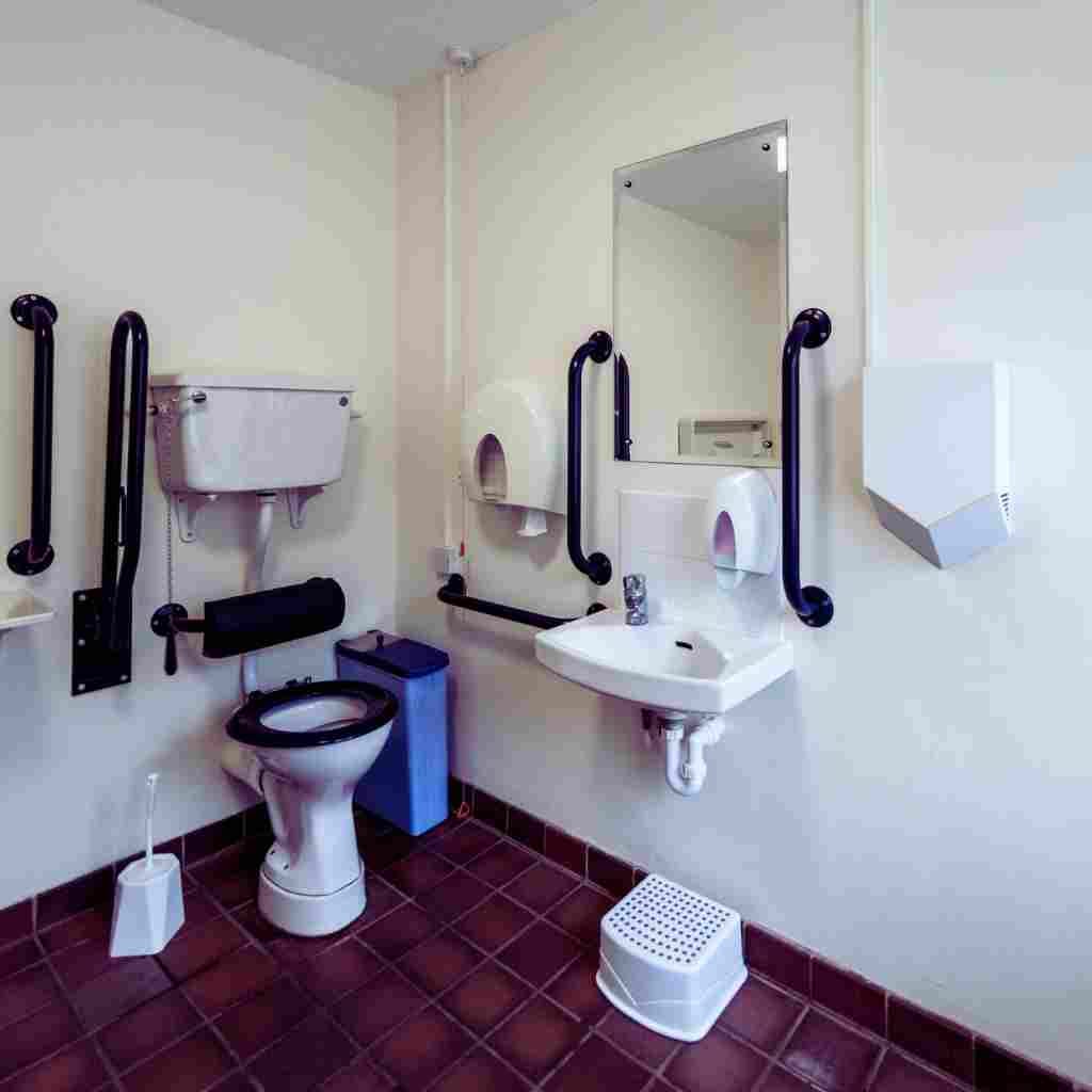 Accessible California restroom with compliant grab bars, wall-mounted sink, insulated pipes, and required clear floor space illustrating ADA and Title 24 bathroom dimension standards.