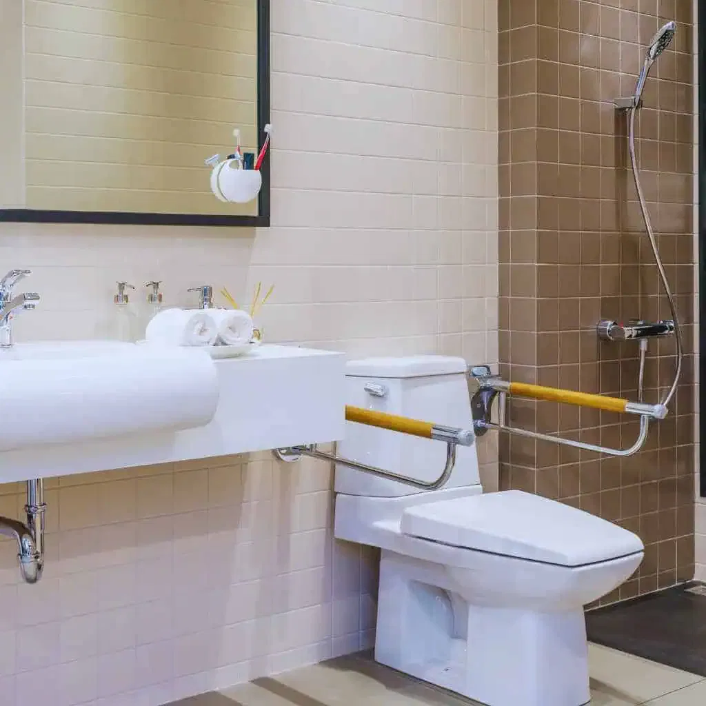 Accessible California bathroom with a wall-mounted sink, insulated piping, folding grab bars at the toilet, and open floor space illustrating ADA and Title 24 fixture dimension requirements.