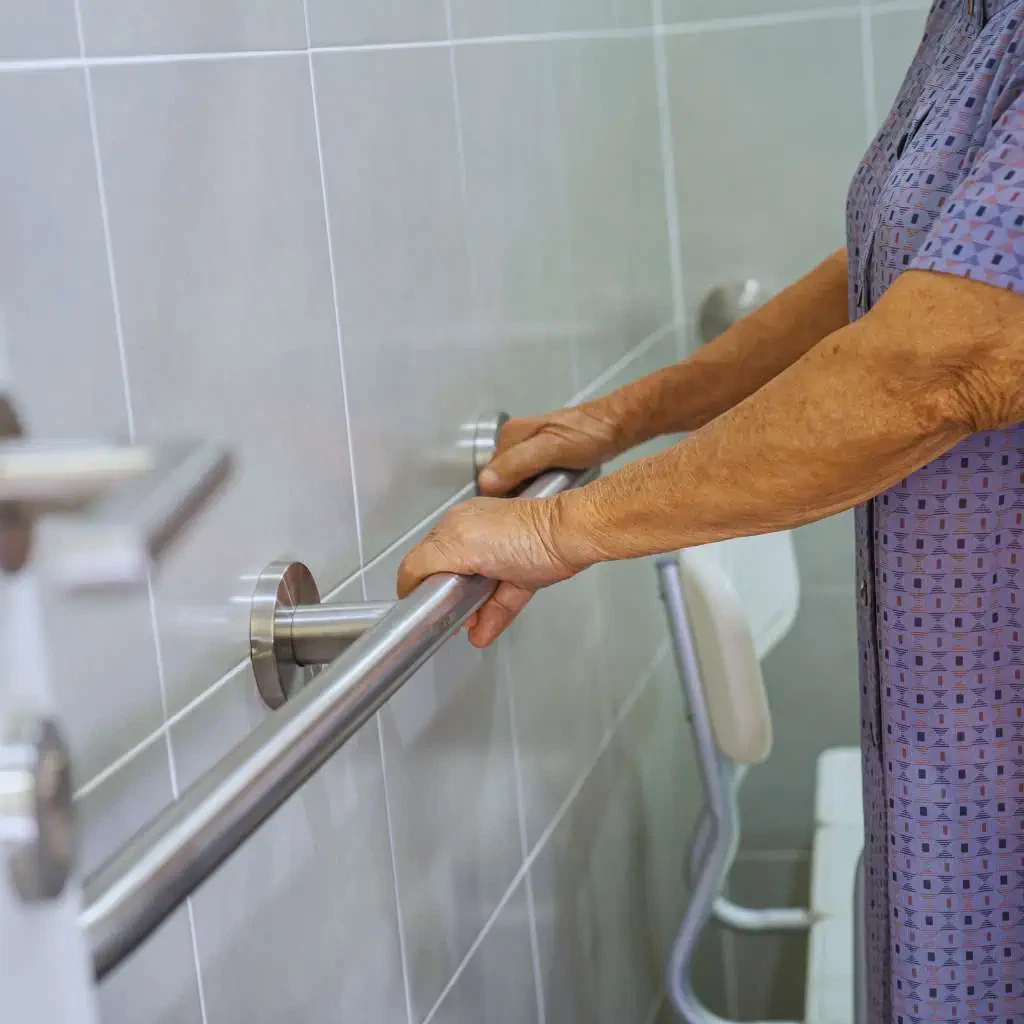 Elderly person gripping an ADA-compliant grab bar in a bathroom, highlighting the required 33 to 36-inch installation height for accessibility.
