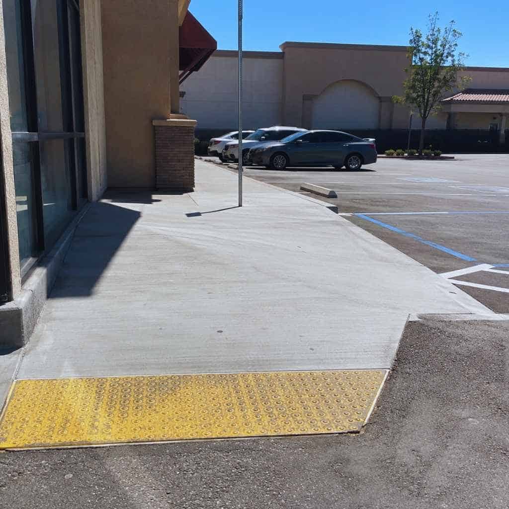 Exterior concrete accessibility ramp at California strip mall entrance showing steep cross-slope and faded tactile warning strip