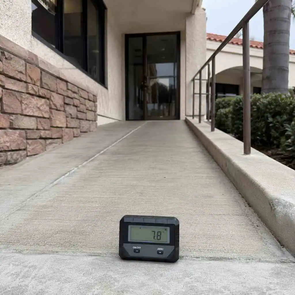 Digital inclinometer on commercial building entrance ramp measuring running slope during CASp accessibility inspection
