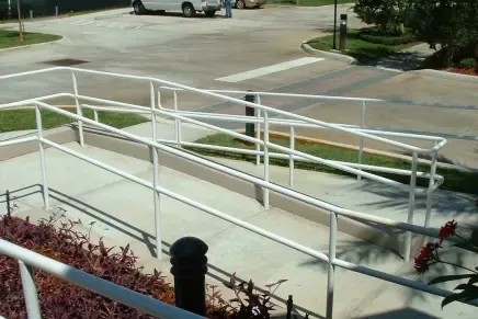 Accessible ramp leading to business entrance with compliant handrails and sidewalk crossing visible in background