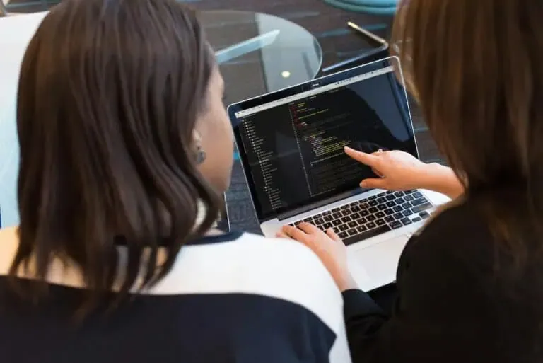 Two women discussing ADA digital compliance while reviewing website code on a laptop