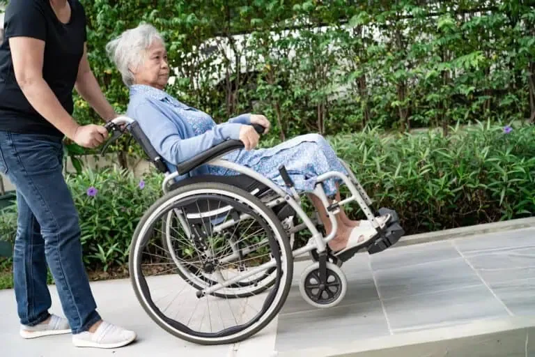 Senior in wheelchair being guided down a compliant ramp with proper slope and edge