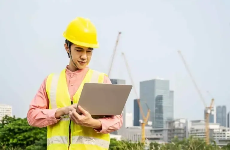 A construction worker wearing safety gear uses a laptop on-site during ADA compliance upgrades at a California government facility