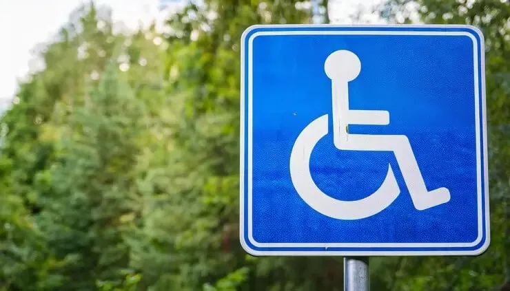 Blue wheelchair-accessible parking sign displayed at legal height near tree-lined area