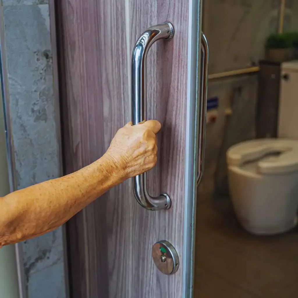 A senior person opening a bathroom door with a metal pull handle in a public restroom, highlighting ADA accessibility concerns relevant to Fresno business compliance