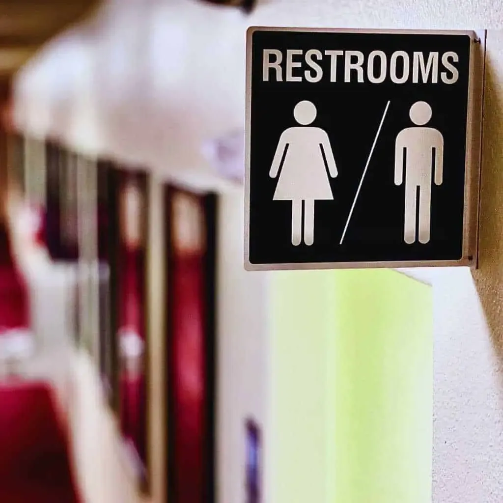 A wall-mounted restroom sign with male and female symbols and no tactile or Braille features, highlighting a common signage issue that fails to meet California Title 24 and ADA requirements for accessible restrooms.