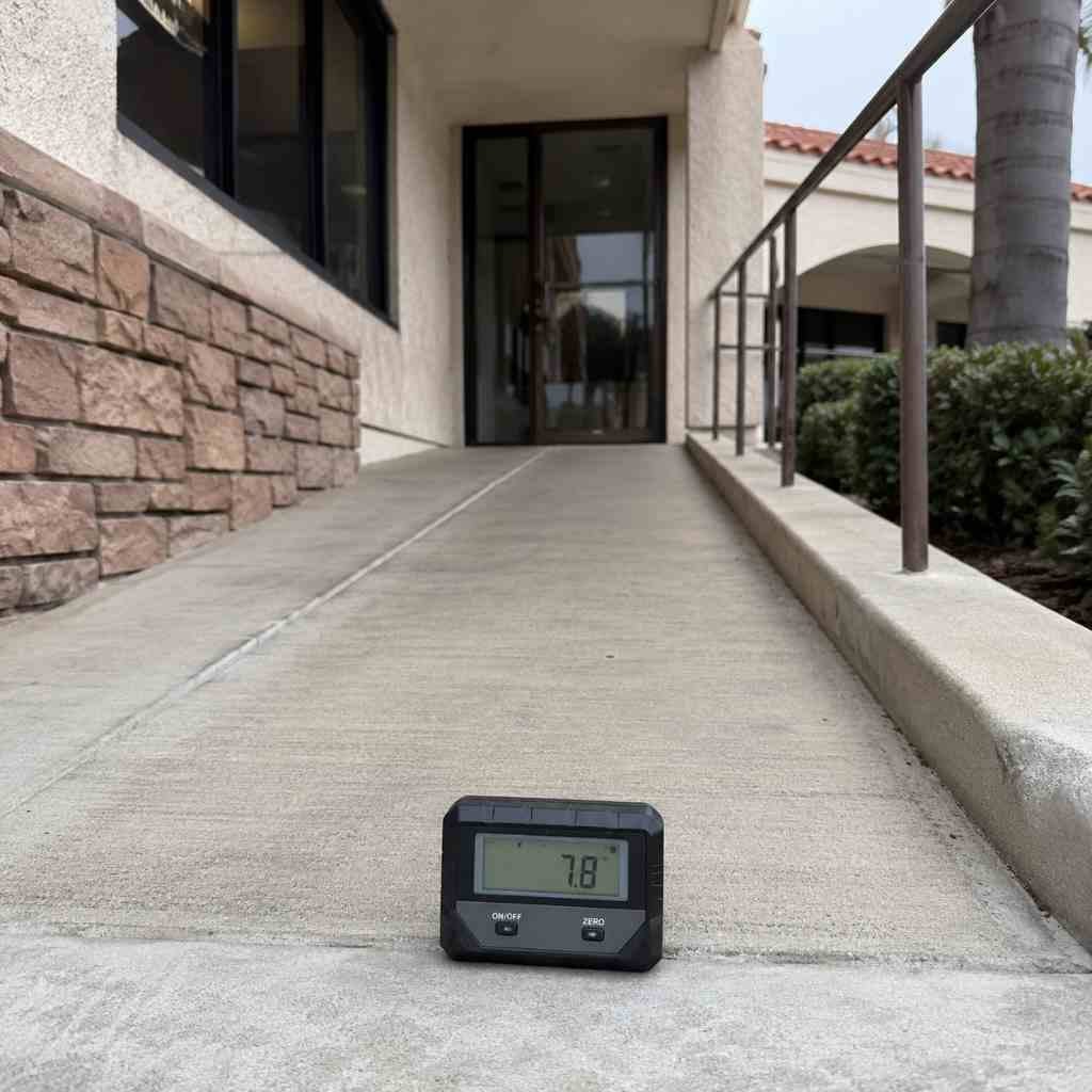 Digital inclinometer on commercial building entrance ramp measuring running slope during CASp accessibility inspection